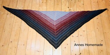 Gehäkeltes Dreieckstuch mit Farbverlauf von Hellblau über Bordeaux zu Dunkelblau und offenem Lochmuster auf hellem Holzboden