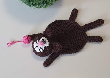 Gehäkelter brauner Katzen-Untersetzer mit rosa Nase und weißen Wangen auf hellem Untergrund
