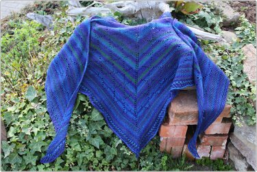Gestricktes blau‑lila Dreieckstuch mit Lochmuster über Ziegeln und Efeu drapiert
