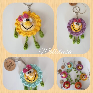 Gelber gehäkelter Blumen-Schlüsselanhänger mit Smiley-Gesicht, rosa Schleife und grünen Beinen; daneben lila, hellblauer und weitere bunte Anhänger.