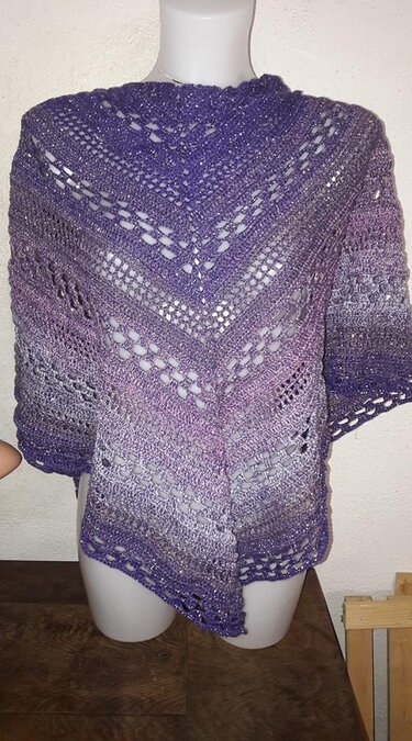 Gehäkeltes Dreieckstuch in Lila‑ und Silbertönen mit eingearbeiteten Glanzfäden und offenem Lochmuster auf Schaufensterpuppe.