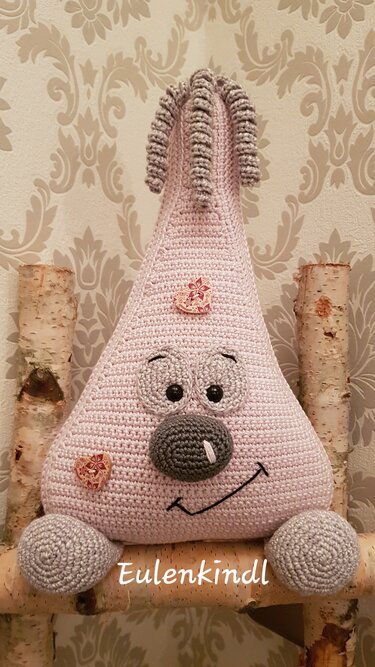 Rosafarbener, dreieckiger Amigurumi-Türstopper mit grauem Gesicht, runden Füßen und Holzknöpfen auf Birkenholzstämmen