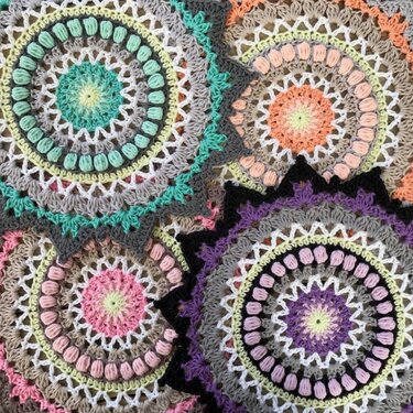 Four circular crochet motifs featuring puff stitches, lace rounds, and star-point edges in pastel shades