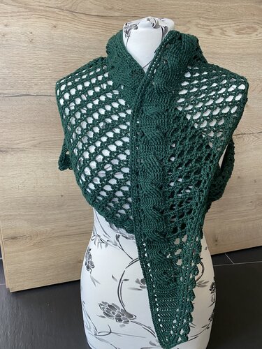 Dunkelgrünes gehäkeltes Dreieckstuch mit Loch- und Zopfmuster auf einer Schneiderpuppe.