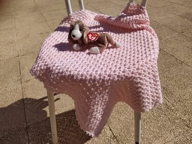 Rosa gehäkelte Babydecke mit waffelartiger Struktur auf einem Stuhl, kleines Plüschhund-Spielzeug darauf
