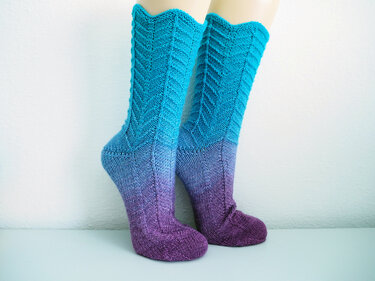 Pair of knitted purple-to-turquoise ombre socks with chevron stitch on mannequin legs.