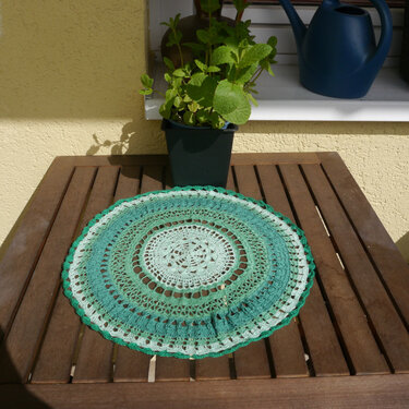 Grünes rundes Häkeldeckchen mit Loch- und Spitzenmustern auf Holztisch