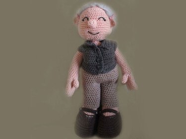 Amigurumi crochet doll of an elderly man with white hair, grey vest, grey pants, and brown shoes, smiling