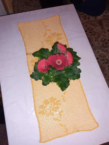 Gehäkelter gelber Tischläufer mit floralem Muster und roten Gerbera auf weißer Tischdecke