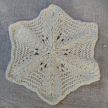 Cremeweiße gestrickte Stern-Applikation mit Lochmuster auf grauem Stoff
