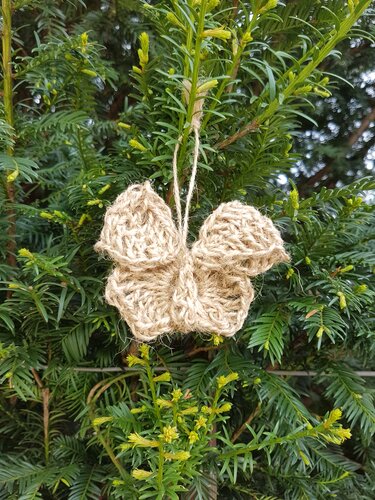 Handgehäkelter Schmetterling aus beigefarbener Jute an einem grünen Ast befestigt