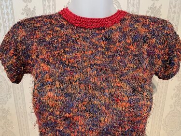 Mehrfarbiges Damen-Kurzarm-Strickshirt aus fransigem Garn in Orange, Blau und Violett mit rotem Rundhalsausschnitt auf Büste