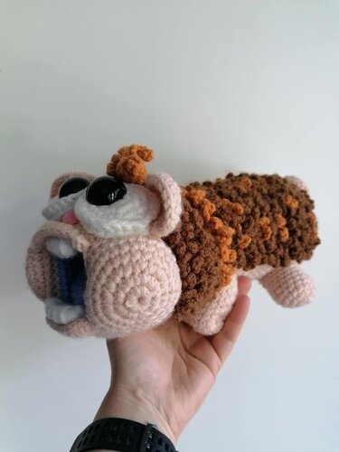 Hand hält gehäkeltes Amigurumi in Braun-, Orange- und Beigetönen mit großen schwarzen Augen und geöffnetem Mund