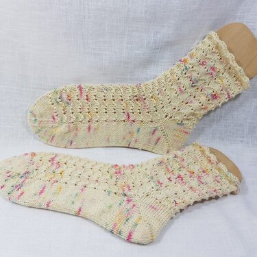 Gestricktes Sockenpaar in Creme mit Lochmuster und bunten Garnsprenkel auf hellem Stoff.