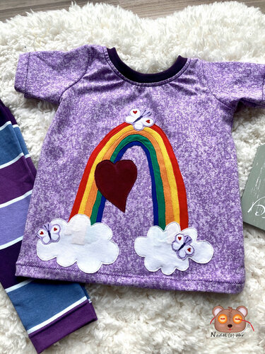 Lila Kindershirt mit appliziertem Regenbogen, rotem Herz, Wolken und Schmetterlingen; gestreifter Hosenrand daneben