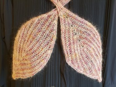 Zwei gestrickte, blattförmige Schalenden aus flauschigem, pastellfarbenem Garn vor dunklem Hintergrund