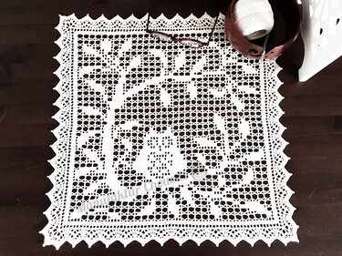 Weißes gehäkeltes Deckchen mit Baummotiv auf dunklem Holztisch
