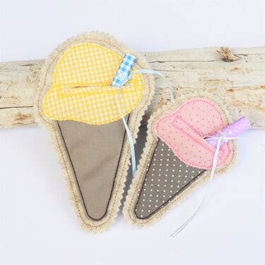 Zwei genähte Stoff‑Eistüten‑Anhänger in Gelb und Rosa mit gezacktem Rand und Bändern.