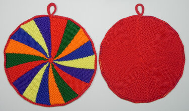 Zwei runde gestrickte Topflappen nebeneinander: links buntes Keilmuster, rechts einfarbig rot, beide mit Schlaufe