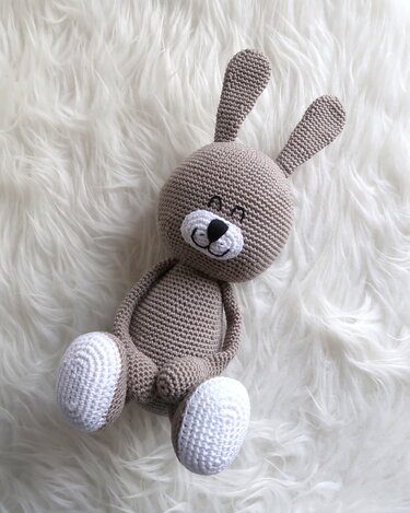 Gehäkelter brauner Amigurumi‑Hase mit weißen Pfoten auf weißem Fell