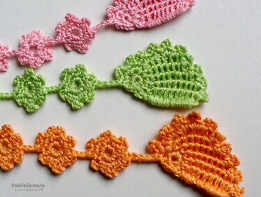Drei gehäkelte Lesezeichen in Rosa, Grün und Orange mit kleinen Blütenketten und blattförmigen Enden.