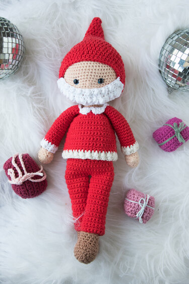 Gehäkelte Amigurumi-Puppe als Weihnachtsmann mit roter Mütze und weißem Bart auf weißem Fell