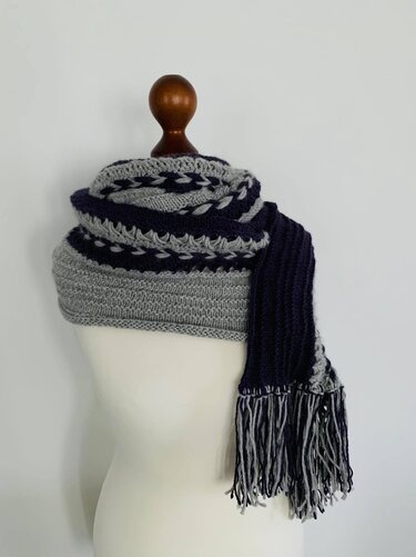 Gestrickter Schal mit abwechselnden Streifen, Zopfreihen und Fransen an einer Schneiderpuppe