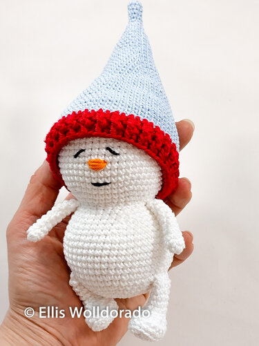 Gehäkelter Amigurumi-Schneemann in einer Hand mit blauer Zipfelmütze und rotem Rand
