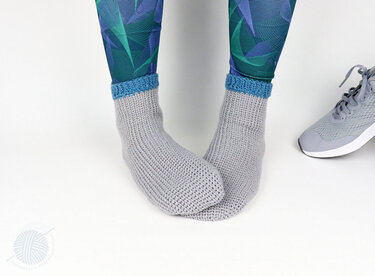 Close-up of grey crocheted ankle socks with blue cuff beside gray athletic shoe