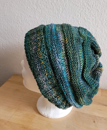 Gestrickte Beanie in Grün- und Blautönen mit mehrfarbigen Akzenten auf weißem Kopfmodell.
