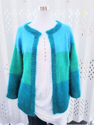 Schaufensterpuppe mit offener Strickjacke in Blau- und Grüntönen über weißer Bluse