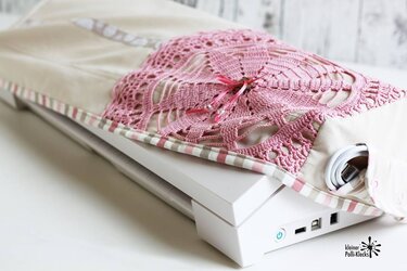 Beige Plotterhülle mit rosa Häkelapplikation, gestreiftem Rand und Seitentasche mit aufgerolltem Kabel