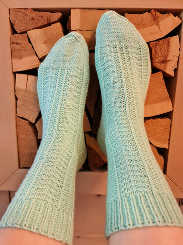 Mintgrüne gestrickte Damensocken mit Ajourmuster auf gestapeltem Brennholz