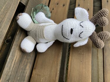 Rentier-Amigurumi aus weißem und braunem Garn liegend auf Holzbrett