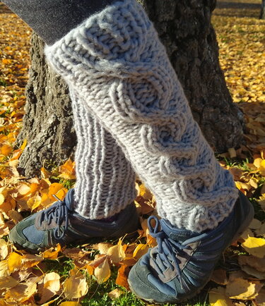 Beinstulpe aus dickem hellgrauem Garn mit Zopfmuster und Rippenbündchen, getragen über Sneakern auf Herbstlaub