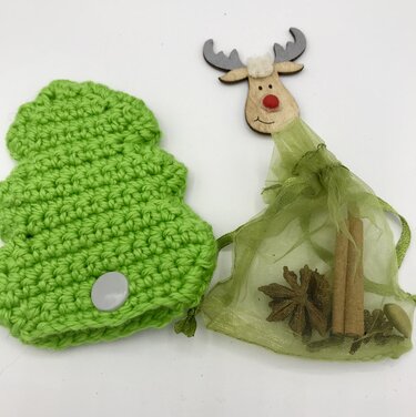 Grünes gehäkeltes Tannenbaum-Täschchen mit Druckknopf neben grünem Organza-Beutel mit Zimtstangen und Sternanis sowie Holzrentier