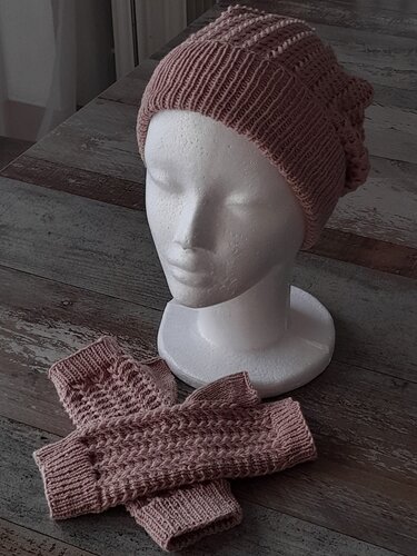 Gestrickte altrosa Mütze auf Schaufensterkopf mit passenden Handstulpen auf Holzfläche
