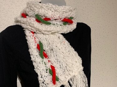 Weißer gestrickter Schal mit roten und grünen Akzenten über schwarzem Oberteil