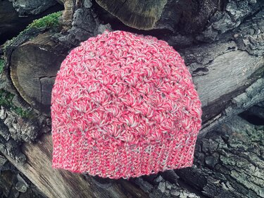 Rosa-weiß-graue gehäkelte Mütze mit strukturiertem Muschelmuster auf Holz