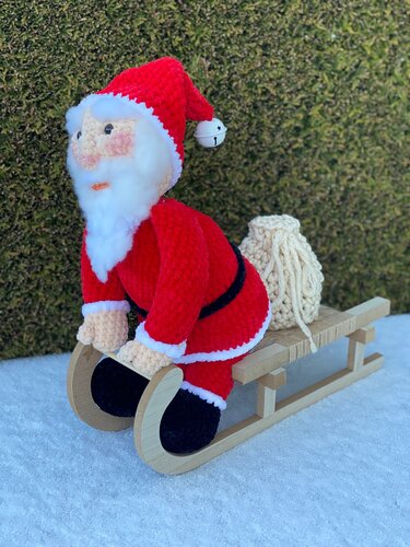 Gehäkelter Weihnachtsmann in roter Kleidung auf Holzschlitten mit Sack