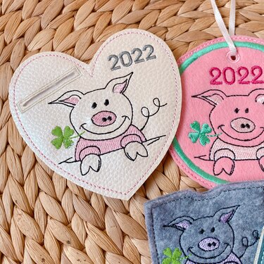 Drei bestickte Glücksanhänger mit Schweinchen, Kleeblatt und Jahreszahl 2022 in Herz- und Rundform in Weiß, Pink und Grau