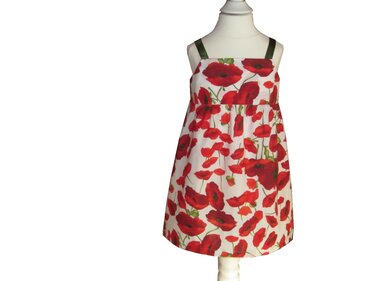 Weißes Kinder-Trägerkleid mit roten Mohnblumen und grünen Trägern auf Schneiderpuppe