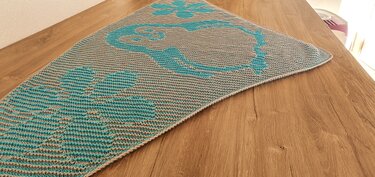 Gestricktes Dreieckstuch in Türkis und Hellgrau mit großen organischen Mustern, flach auf Holztisch