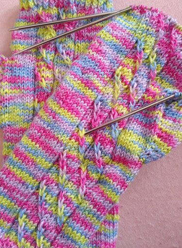 Unfertiges gestreiftes Strickstück für Armstulpen mit Glitzergarn und Stricknadeln