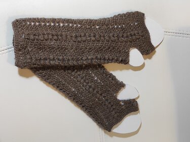 Dunkelbraune, fingerlose Häkelhandschuhe mit Lochmuster auf hellem Untergrund