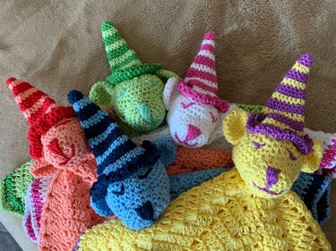 Mehrere gehäkelte Babyschmusetücher mit Tierköpfen und gestreiften Zipfelmützen in verschiedenen Farben auf hellem Untergrund