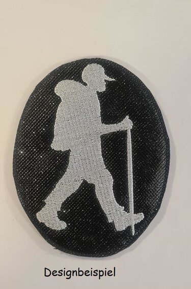 Ovales Stickmotiv mit heller Silhouette eines Wanderers mit Rucksack und Wanderstock auf dunklem Grund