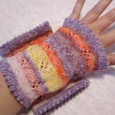Gestrickter fingerloser Armstulpen mit bunten Streifen, Lochmuster und gewelltem Rand auf einer Hand.