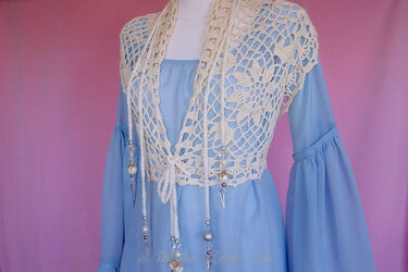 Cremefarbene gehäkelte Weste mit Lochmuster und perlenbesetzten Bändern über einem hellblauen Kleid auf einer Schaufensterpuppe.