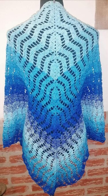 Detail eines gehäkelten Dreieckstuchs mit rhythmischem Wellen‑Lochmuster und Farbverlauf in Blau, drapiert auf Mannequin